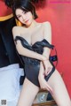 A woman in a black bodysuit posing on a bed.