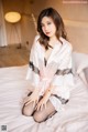 A woman sitting on a bed wearing a pink robe.
