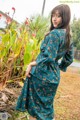 A woman standing in front of a bush wearing a green dress.