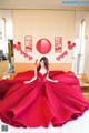 A woman in a red dress sitting on a bed.