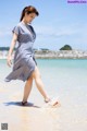 A woman in a blue and white dress walking on the beach.