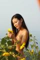 A naked woman standing in a field of sunflowers.